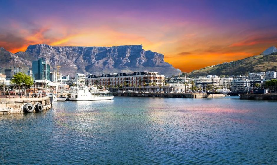Cape Town waterfront at sunset with Table Mountain rising behind the harbor and city skyline. Displaying the natural beauty that inspires the Den of Luxe founder.